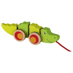 Green wooden toy crocodile with red and yellow wheels on a white background